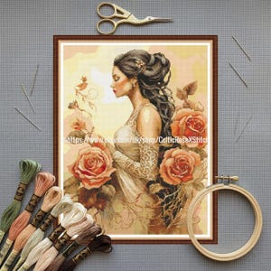 Puede incluir: Un bordado de punto de cruz enmarcado de una mujer con un vestido blanco y rosas naranjas. Hilos de bordar, agujas, tijeras y un bastidor se colocan alrededor del marco. El texto en la imagen dice: https://www.etsy.com/uk/shop/CelticRoseXStitch