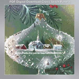 May include: A PDF digital download cross stitch pattern featuring a clear glass ornament hanging from a pine branch. Inside the ornament is a winter village scene with a church and small houses. The text reads PDF Digital Download Cross Stitch Pattern.