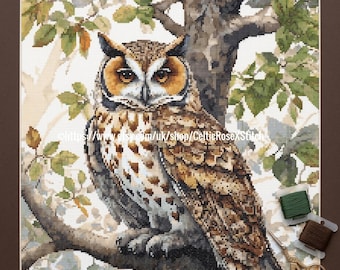 May include: A PDF digital download cross stitch pattern featuring a long-eared owl perched on a tree branch with green leaves. The design includes detailed brown, tan, and white feathers. Two spools of embroidery thread and gold scissors are visible.