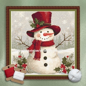May include: Cross-stitch artwork of a snowman wearing a red top hat, scarf, and mittens. The snowman has a carrot nose, coal eyes, and a twig mouth. The background shows a snowy winter scene with evergreen trees and falling snow. The artwork is framed in a brown wooden frame.