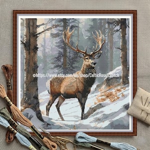 May include: Cross-stitch artwork of a majestic deer in a snowy forest scene, framed in a brown wooden border. The deer has large antlers and is surrounded by trees and snow. The image includes embroidery floss and scissors.