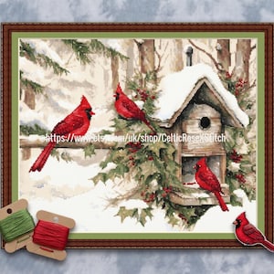 May include: Cross-stitch artwork of red cardinals perched on snow-covered branches near a birdhouse. The scene is set in a winter landscape with a brown wooden frame. Green and red thread spools are in the lower left corner.