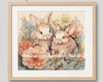 May include: A PDF digital download cross stitch pattern featuring two light brown rabbits nestled among large peach and orange flowers with green leaves. The image is framed in a light wood frame and includes the text PDF Digital Download Cross Stitch Pattern.