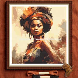 May include: Framed cross-stitch portrait of a woman with a head wrap, earrings, and a patterned top. The artwork features warm tones of brown, orange, and beige. The frame is dark brown. The image includes thread spools and a decorative African continent pin.