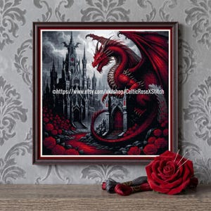 May include: Framed cross-stitch art depicting a red dragon and a gothic castle. The dragon has large wings and is set against a dark, stormy sky. Red roses and a red path lead to the castle. The Etsy shop URL is visible.