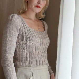 May include: A light brown knitted sweater with a square neckline and long sleeves. The sweater has a ribbed texture and is cropped.