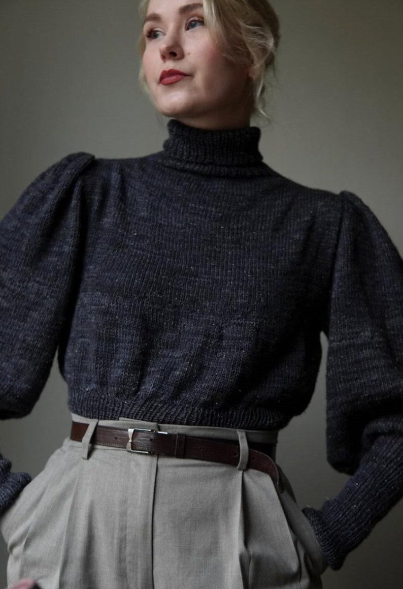 May include: A dark gray turtleneck sweater with puffed sleeves and a brown leather belt. The sweater is made of a soft, textured fabric.
