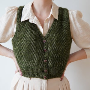 May include: A green knitted vest with a V-neck and button closure. The vest is made of a textured yarn and has a casual, relaxed fit.