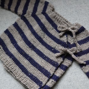 Könnte beinhalten: Ein gestreifter Strickpullover für Babys mit blauen und grauen Streifen und einem Schleifendetail.