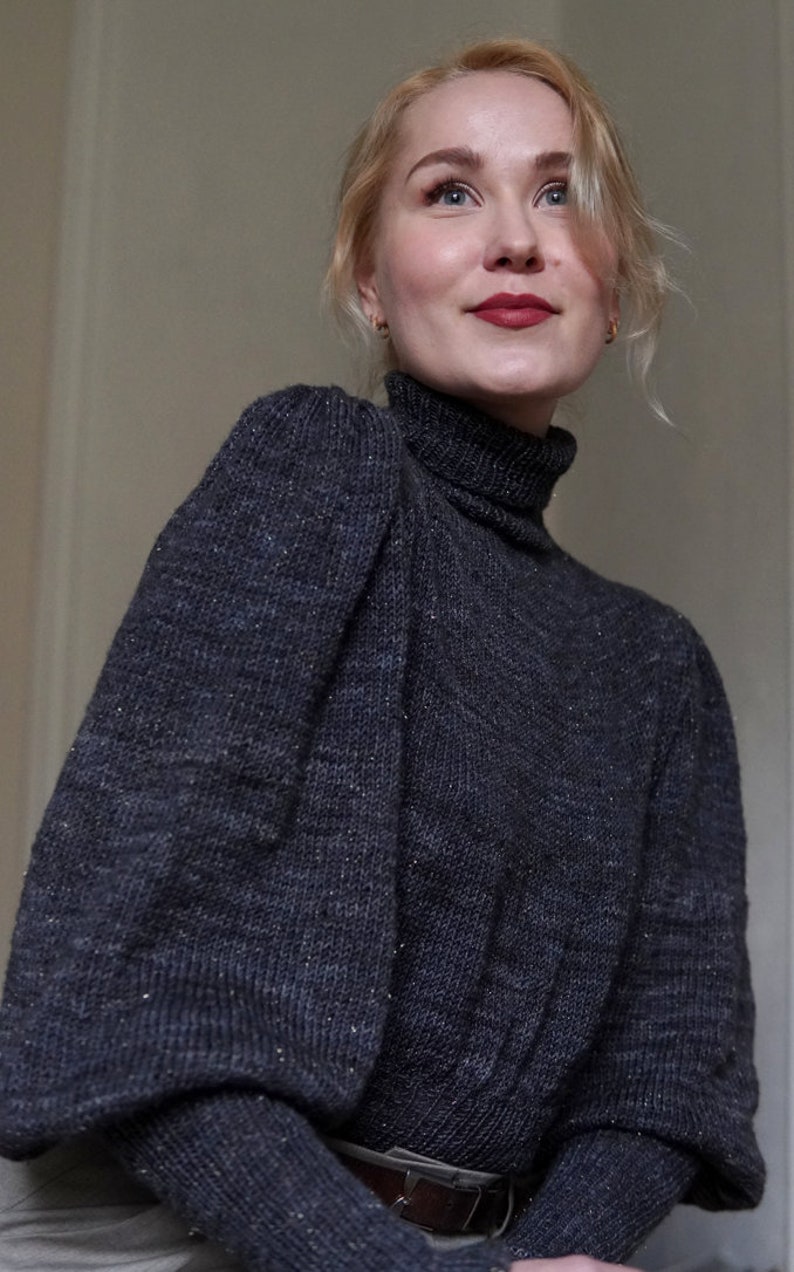 May include: A woman wearing a dark gray turtleneck sweater with puffed sleeves. The sweater has a subtle sparkle throughout the fabric.