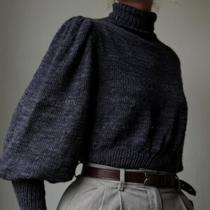 May include: A dark gray turtleneck sweater with puffed sleeves and a brown leather belt. The sweater is made of a soft, textured fabric.