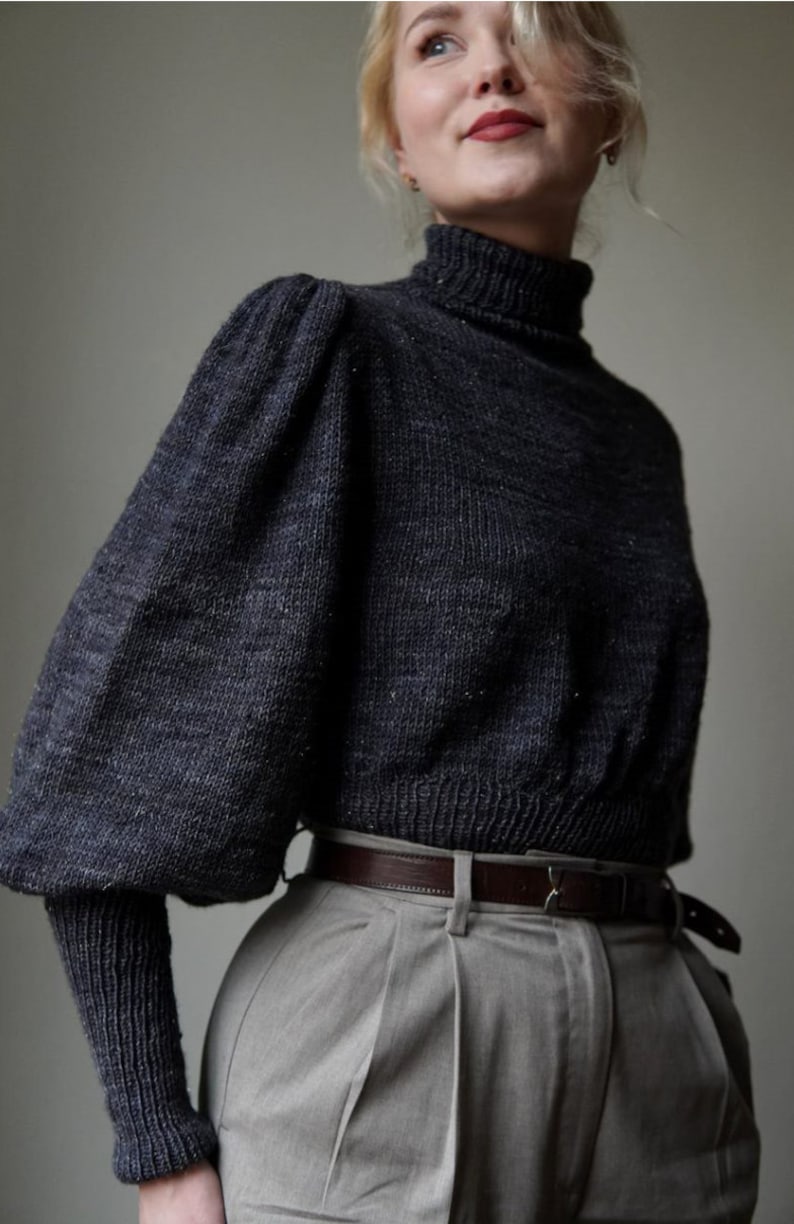 May include: A dark gray turtleneck sweater with puffed sleeves and a brown leather belt. The sweater is made of a soft, textured fabric.