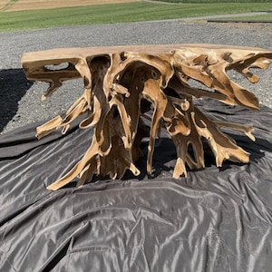 May include: A natural wood console table with a unique, organic design. The table features a thick, rectangular top supported by a complex network of intertwined wooden roots, creating a sculptural and artistic base. The table is approximately 60 inches long.