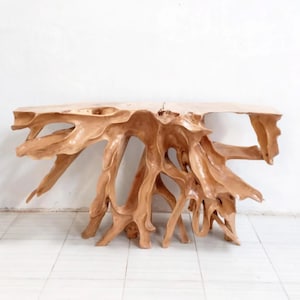 May include: A natural wood console table with a unique root-like base. The light brown table has a smooth, rectangular top and an intricate, organic design. The base is made of intertwined wooden roots, creating an eye-catching, sculptural piece.