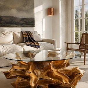 May include: A coffee table featuring a clear, oval-shaped glass top supported by a large, natural light-brown wooden tree root base. The base displays intricate, organic textures and curves, providing a sturdy foundation for the glass surface.
