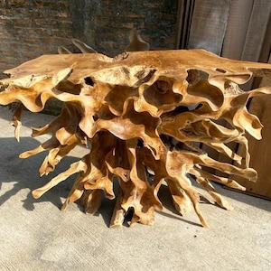 May include: A unique, freeform wooden table with a natural, organic design. The table features a light brown color and a complex, root-like base. The top surface is smooth, while the base has intricate, flowing shapes.