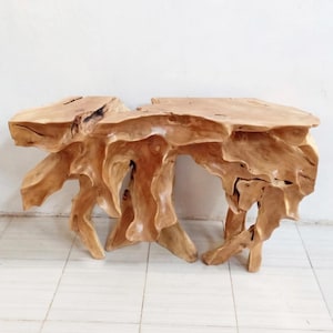 May include: A natural wood console table with a unique, organic design. The table features a light brown color and a textured surface, with a freeform shape. The table's base has an open, sculptural design.