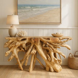 May include: A natural wood console table with a unique root-like base. The table is topped with a lamp, coral, and a bowl of stones. A framed beach scene painting hangs above the table. A woven basket sits on the floor.