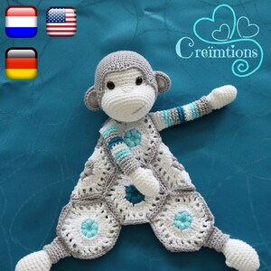 May include: A handmade crochet monkey security blanket in gray, white, and blue. The monkey has a gray head and arms, a white face and hands, and a patterned body with blue accents. The text "Kleine-Knuffel-Aap" is at the bottom.