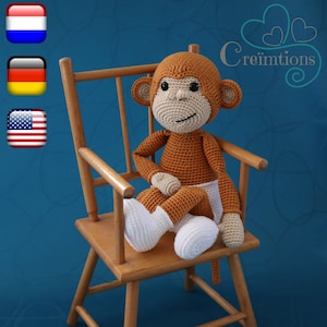 Può includere: Un giocattolo di scimmia all'uncinetto seduto su una sedia di legno. La scimmia è marrone con accenti bianchi e indossa un pannolino. La sedia è una seggiolone con uno sfondo blu.