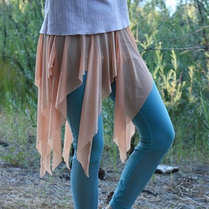 May include: A woman is wearing a light pink skirt with a blue and white striped pattern. The skirt is layered and has a flowing design. The woman is also wearing blue leggings.