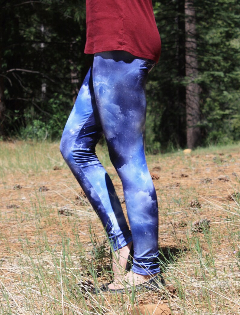 May include: Blue leggings with a galaxy print. The leggings have a dark blue background with white and light blue cloud-like patterns, creating a celestial design. The leggings are worn with a maroon top.