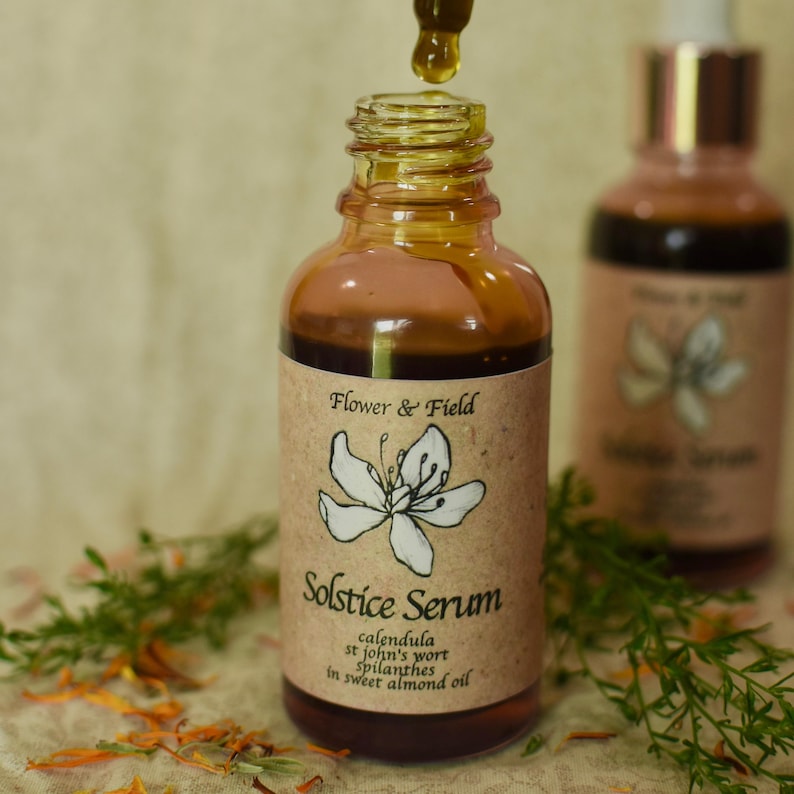 以下が含まれることがあります： ドロッパーで液体を出すSolstice Serumの茶色のガラス瓶。ラベルには「Flower & Field」と「Solstice Serum」と書かれており、植物のイラストと成分の詳細が記載されています。セラムは琥珀色です。