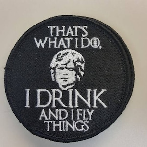May include: Black embroidered patch with white text and a portrait. The text reads "THAT'S WHAT I DO, I DRINK AND I FLY THINGS". The portrait is of a man with short hair. The patch is round.