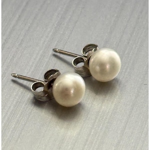May include: A pair of pearl stud earrings. Each earring features a round, creamy white pearl set on a silver post with a butterfly backing. The earrings are displayed on a light gray surface.