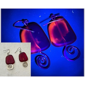 May include: A pair of red and silver earrings. The earrings have a rectangular red glass stone with a silver spiral design below. The earrings are displayed on a blue background with a close-up of the earrings.