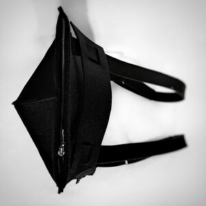 May include: A black tote bag made of felt, featuring a zippered closure and two long straps. The bag is open, revealing the interior. The design is simple and modern, with a focus on functionality and a minimalist aesthetic.