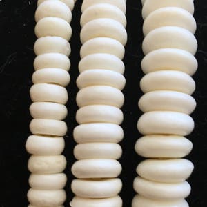 以下が含まれることがあります： オフホワイトの丸いビーズが3連。ビーズはサイズと形が均一で、組み合わせてテクスチャード加工されたレイヤー効果を生み出しています。背景は無地の黒で、ビーズとのコントラストを際立たせています。