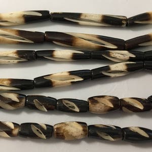 Könnte beinhalten: Eine Kette aus braunen und weißen Knochenperlen mit einem wirbelnden Muster. Die Perlen sind zylindrisch und haben eine glatte, polierte Oberfläche.