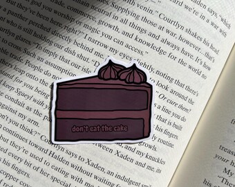 May include: A sticker of a chocolate cake with pink frosting and the text "don't eat the cake" on it. The sticker is placed on a page of a book.