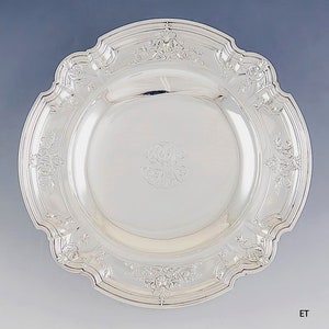 May include: A silver serving bowl with a scalloped edge and an ornate design. The bowl has a monogram in the center.
