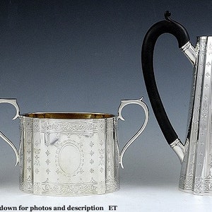 Op de afbeelding: Een zilveren theeservies met een theepot, roomkan en suikerpot. De set is versierd met een ingewikkeld bloemmotief en heeft een gepolijste afwerking.