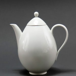 May include: A white porcelain teapot with a rounded, egg-shaped body and a lid with a small knob on top. The teapot has a spout on one side and a handle on the other.