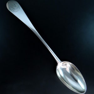 Può includere: Un cucchiaio d'argento con un manico lungo e una ciotola arrotondata. Il manico è inciso con un monogramma.