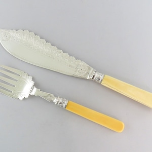 May include: A set of silver-plated serving utensils with ivory handles. The knife has a scalloped edge and the fork has a decorative design.