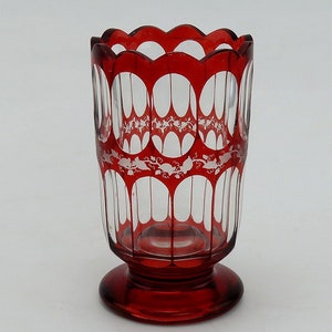 May include: A red glass goblet with a white etched design. The goblet has a scalloped rim and a round base.