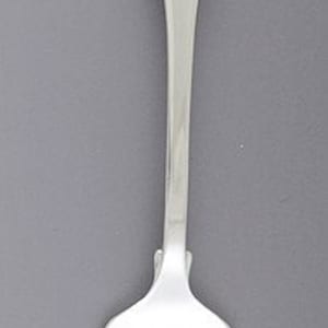 May include: A silver fork with a long, slender handle and four tines. The handle has a rounded end. The fork is made of a shiny, reflective metal and is set against a gray background. The fork is a piece of silverware.