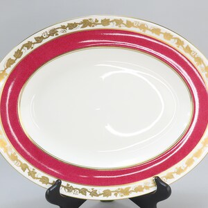 May include: A large oval serving dish with a red rim and a gold floral design. The dish is made of white porcelain.