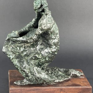 May include: A bronze sculpture of a person kneeling with their head bowed, the sculpture is on a wooden base.
