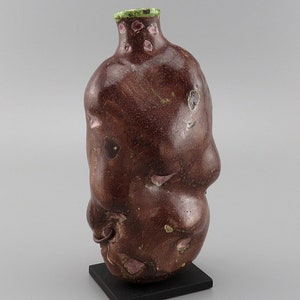 May include: A brown ceramic vase with a green rim and pink speckles. The vase has an organic, asymmetrical shape.