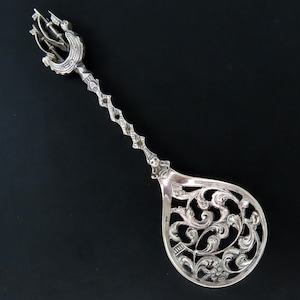 May include: A silver spoon with an ornate, openwork design. The handle is decorated with a detailed, three-dimensional figure of a ship.