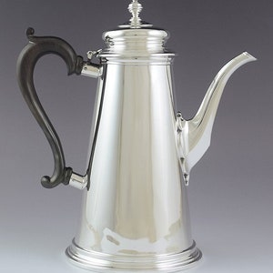 Könnte beinhalten: Eine silberne Kaffeekanne mit einem Holzgriff. Die Kanne hat einen runden Korpus und einen Ausguss an der Seite. Der Deckel hat einen Knauf oben.