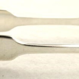 Può includere: Pinzette per lo zucchero in argento con un design arrotondato a forma di cucchiaio. Le pinzette sono in argento lucido e hanno un design semplice ed elegante.