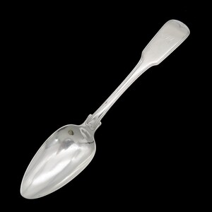 May include: A silver spoon with a rounded bowl and a long, slender handle. The handle is engraved with the initials "A.M."