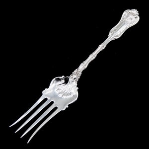 May include: A silver fork with an ornate handle and three prongs. The fork is polished and shiny.