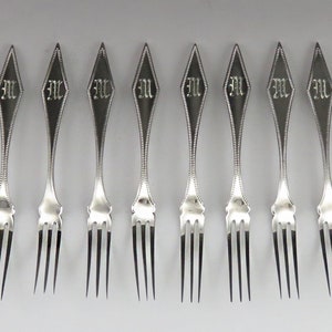 May include: Set of ten silver forks with diamond-shaped handles. Each handle is engraved with the letter "M".